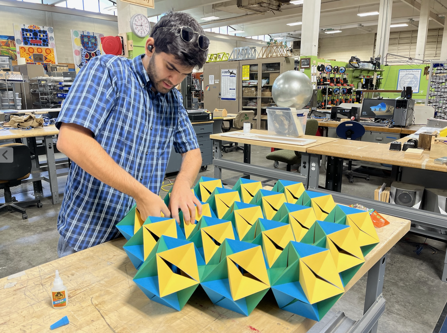 Photo of a researcher assembling a folded, faceted geometric paper structure on a workshop table, part of NASA Space Grant research into material behavior under stress.